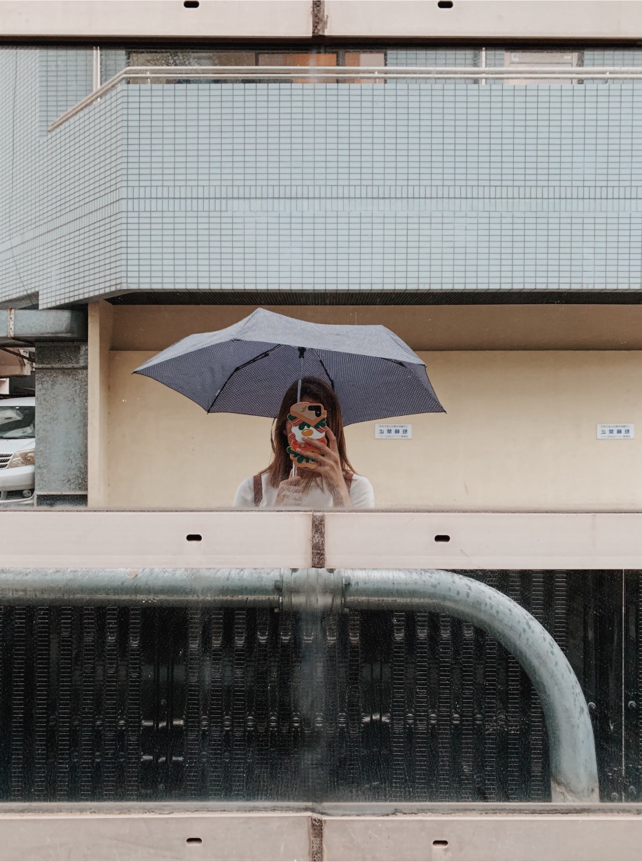 Kat Borchart taking a picture in a mirror on the street of Tokyo with an umbrella